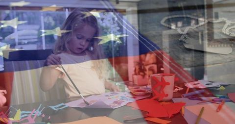 Little girl painting patriotic craft at table with american flag overlay, military tribute