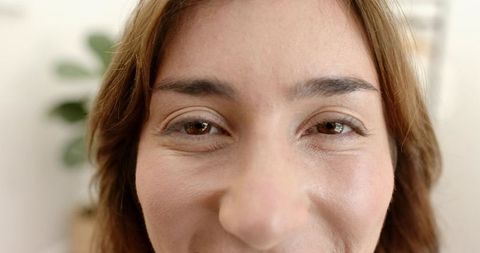 Smiling woman showing natural skin texture and fine lines, warm brown eyes, skincare focus