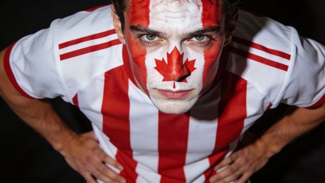 Leaning canadian fan wearing maple leaf face paint and red white jersey, intense close-up