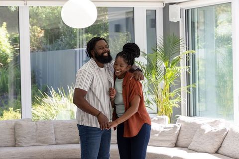 Smiling couple embracing in bright modern living room with glass doors and plants