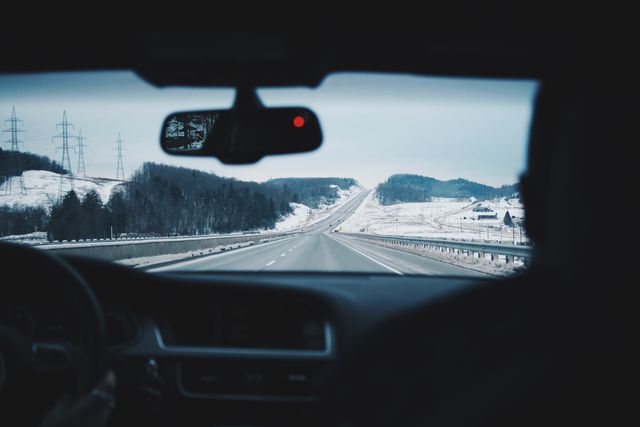 Depicts interior view of car driving through snow-covered landscape, perfect for illustrating winter travel, road safety, or transportation topics. Useful for travel brochures, winter safety guides, or automotive advertisements.