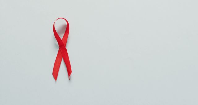 Red ribbon symbolizing AIDS awareness on a white background, perfect for healthcare campaigns, medical awareness events, and educational purposes. Useful for creating promotional materials for HIV/AIDS diagnosis, prevention, support campaigns, and World AIDS Day observance.