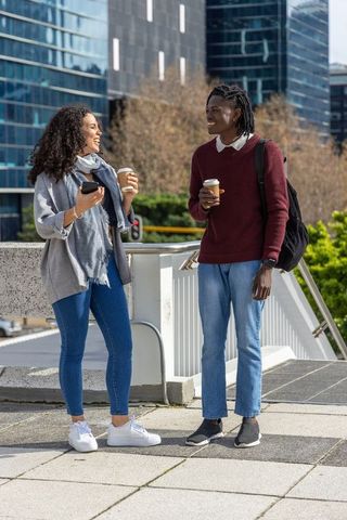Diverse coworkers chatting on urban bridge holding takeaway coffee cups and smartphone