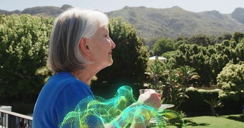 Senior woman enjoying tea on balcony with digital hologram overlay and sunny mountain view