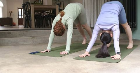 Two Women Practicing Downward Dog at Home on Green Mats for Yoga Wellness