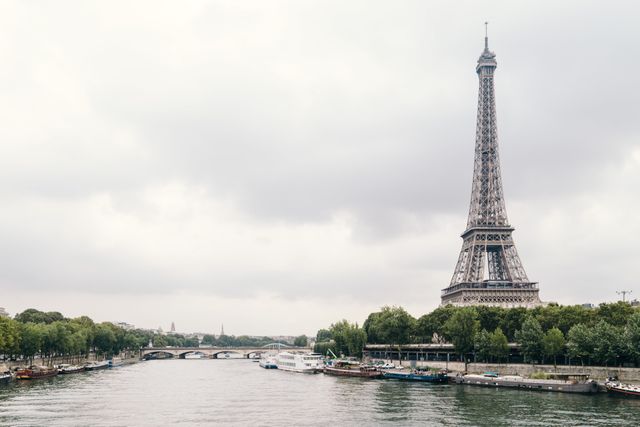 Eiffel Tower standing tall by Seine River on a cloudy day in Paris, France. Ideal for travel blogs, tourism websites, postcards, and promotional materials about French architecture and famous landmarks.