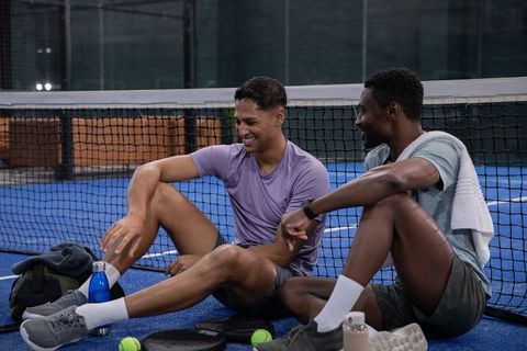 Diverse male athletes sitting on indoor paddle court chatting and cooling down