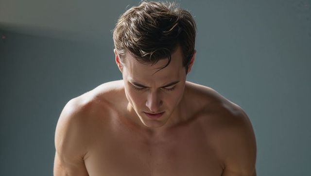 Muscular male model posing bare-chested, tilting head down, sculpted torso, studio lighting
