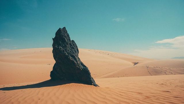 Lonely Rock Formation Amidst Rippling Sand Dunes in Expansive Arid Desert