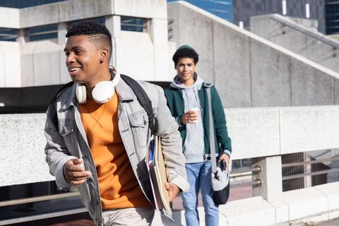 Smiling african american teen student walking urban campus with headphones and notebooks