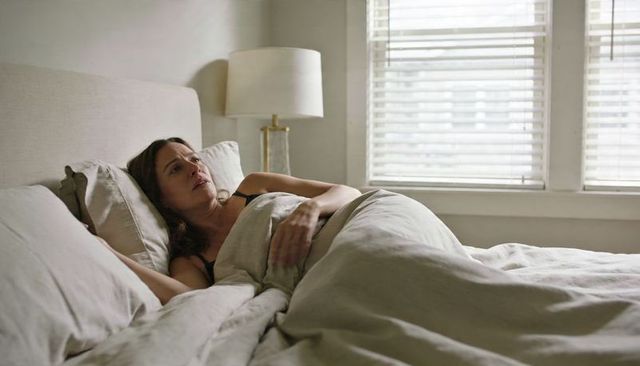 Woman Lying in Bed Resting under Neutral Bedding by Window Blinds Morning Light