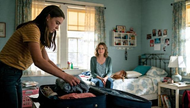Teenager packing suitcase in cozy bedroom while parent watches preparing for weekend trip