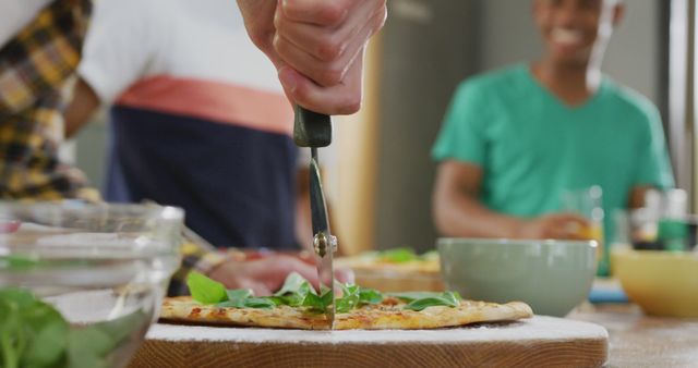 People are sharing a homemade pizza in a modern kitchen. One person is cutting the pizza while others are smiling and enjoying their time. This image can be used for promoting social gatherings, cooking at home, recipes, and lifestyle blogs.