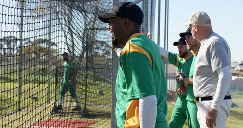 Baseball team watching batting practice through cage cheering and coaching on field