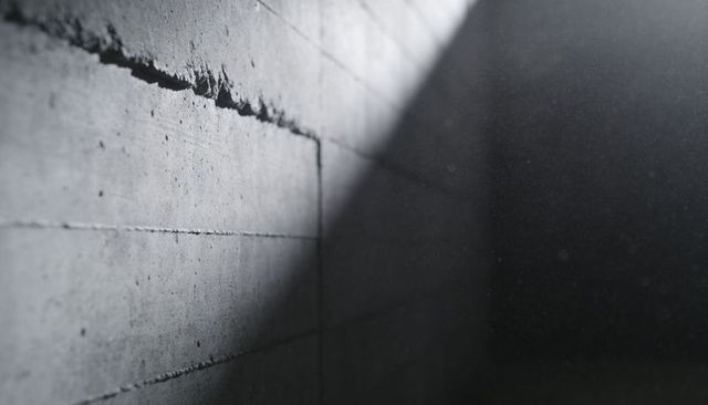 Diagonal light cutting across textured concrete bunker wall with dramatic shadowed void