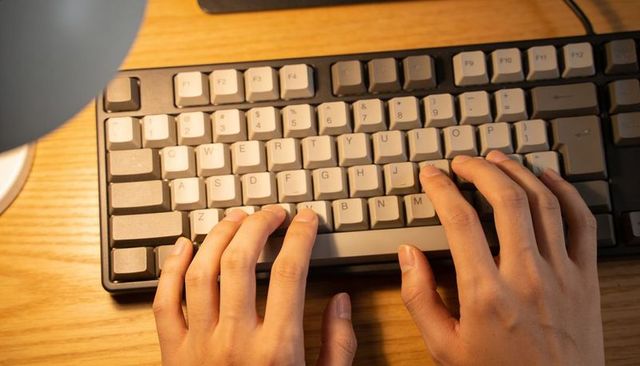 Hands typing on compact mechanical keyboard under warm desk lamp, late night writing