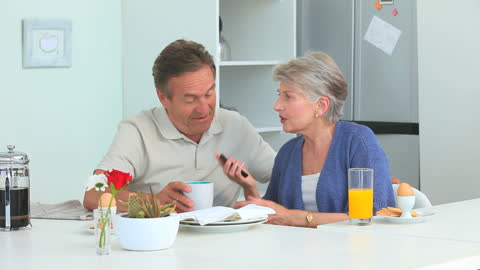 Senior Couple Enjoying Morning Beverage While Taking Phone Call