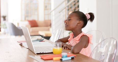 African american girl studying on laptop at dining table with orange juice