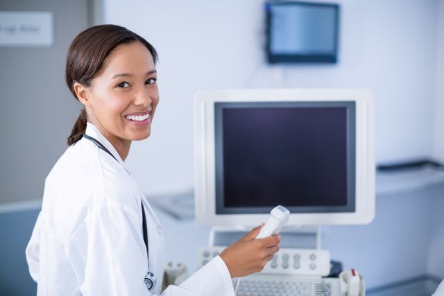 Smiling doctor using ultrasound machine in hospital. Ideal for healthcare, medical technology, and hospital-related content. Can be used in articles, brochures, and websites focusing on medical diagnostics, patient care, and healthcare professionals.