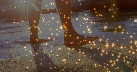 Walking barefoot along sunlit shoreline wading in shallow water with golden bokeh glow