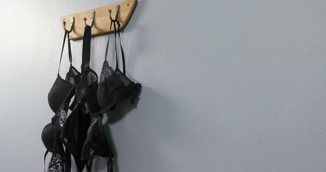 Several black bras hang from hooks on a wooden rack against a white wall, with copy space. This setting suggests a personal space where intimate apparel is organized and stored.