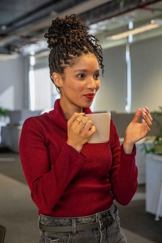 Young african american woman sipping coffee and gesturing during casual modern office conversation