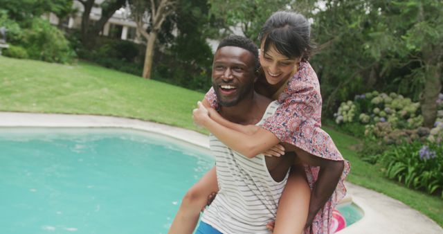 Happy diverse couple at swimming pool, man carrying woman in garden. spending time together at home.