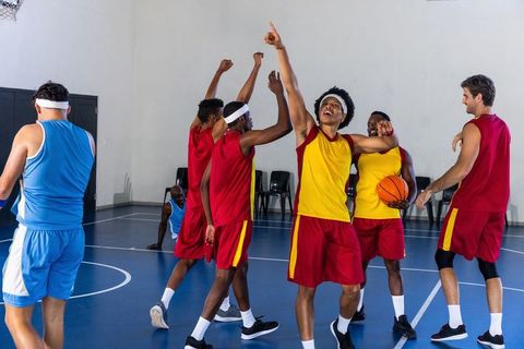 Diverse basketball team celebrating victory on blue indoor court