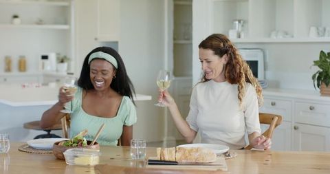 Diverse Friends Toasting Wine and Sharing a Meal in Rustic Kitchen