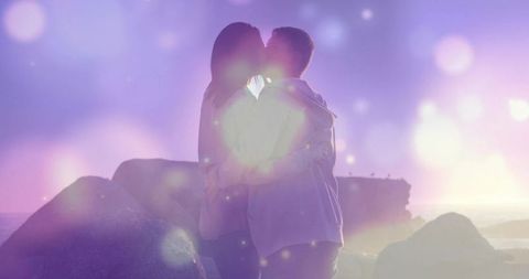 Romantic Couple Embracing and Kissing on Rocky Shoreline at Sunset with Dreamy Lens Flare