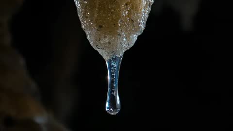 Slow-motion macro video of droplet dripping from cave mineral tip, filament and bubbles