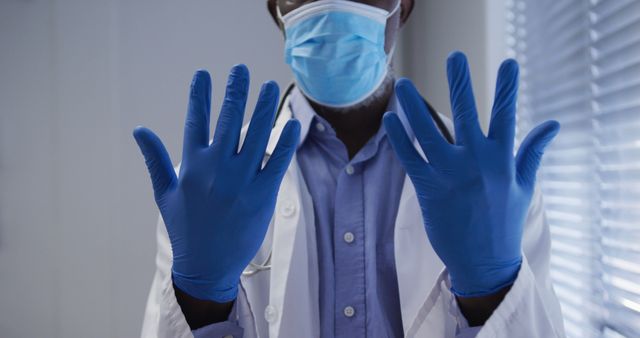 Midsection of biracial male doctor wearing face mask and surgical gloves. medicine, health and healthcare services during coronavirus covid 19 pandemic.