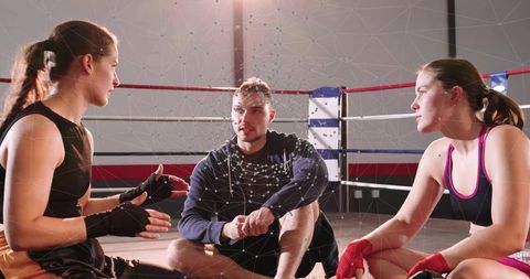 Boxing coach briefing two female boxers in ring during intense training session
