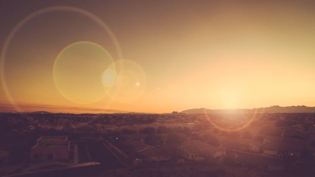 Urban landscape showing housing area at sunset, brilliant sun setting behind mountains, and distinct lens flare adds artistic touch. Ideal for real estate promotions, evening relaxation themes, nature-related content, background images for websites, urban planning presentations, and articles on suburban living.