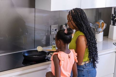 African american mother and teenage daughter cooking on induction stove in modern kitchen