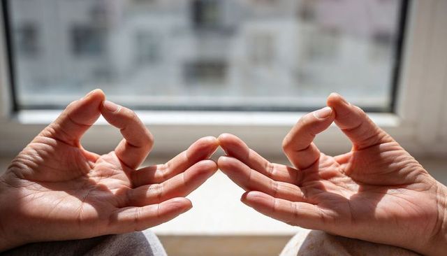 Sunlit hands holding meditation mudra at window sill for mindfulness, calm, reflection