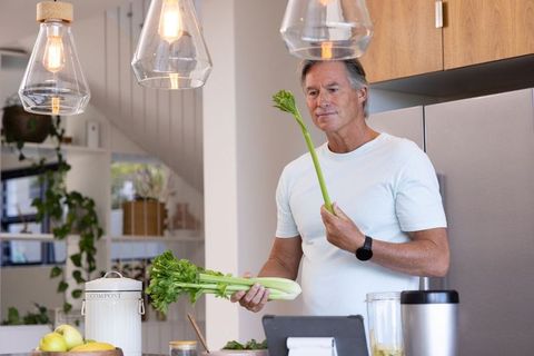 Senior man preparing healthy snack inspecting celery stalk in modern open-plan kitchen