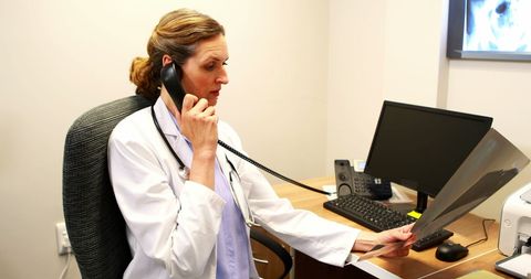 Female Doctor Analyzing X-Ray While on Telephone