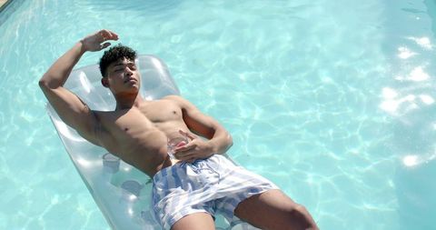 African american man reclining on inflatable lounger in sunlit pool holding drink