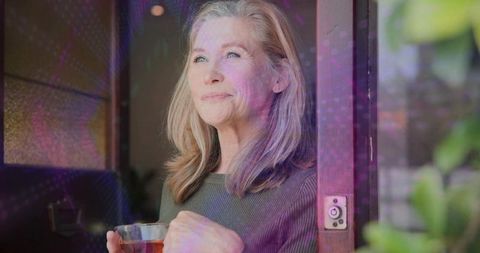 Serene mature woman holding tea in doorway reflecting on morning light and home calm