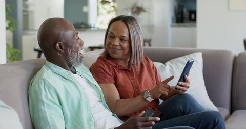 Mature couple relaxing on sofa sharing smartphone moment, laughing and connecting
