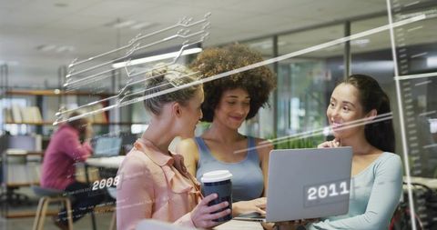 Young professionals collaborating around laptop in modern coworking space holding travel coffee cup