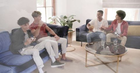 Four friends playing console game on sofas in bright living room, weekend competition