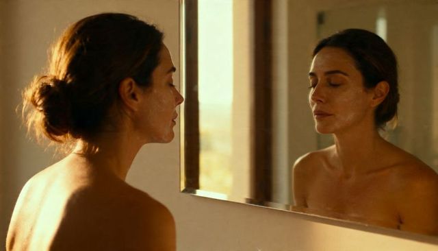 Sunlit woman standing before mirror with facial cream, serene skincare ritual
