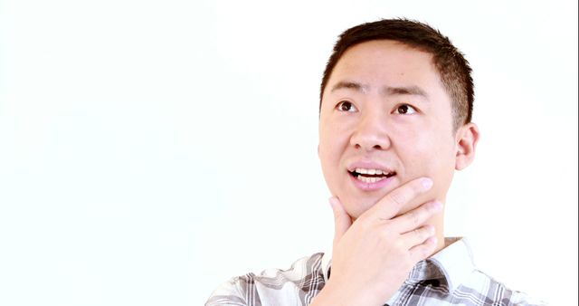 A young Asian man appears pensive, touching his chin in thought, with copy space. His expression suggests he is contemplating a decision or idea.
