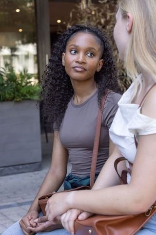 Diverse friends chatting on urban bench holding brown leather bags casual conversation