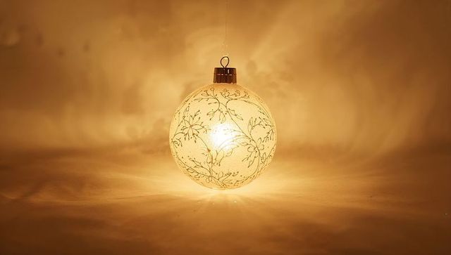 Golden glass bauble hanging with floral vine pattern and warm glowing light holiday ornament