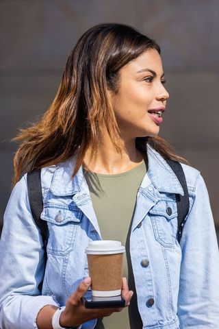 African american woman holding coffee cup on smartphone while walking in denim jacket