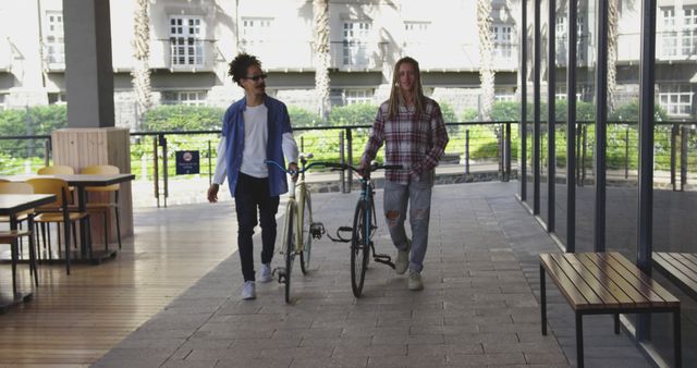 Two diverse male friends walking in the street with bicycles. green urban lifestyle, out and about in the city.