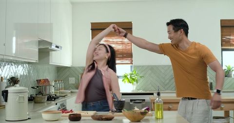 Couple twirling and chopping vegetables on modern kitchen island, playful home cooking